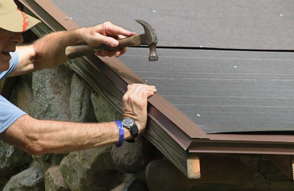 Person using a stabilized ladder to attach outdoor lights along a roof edge with clips.